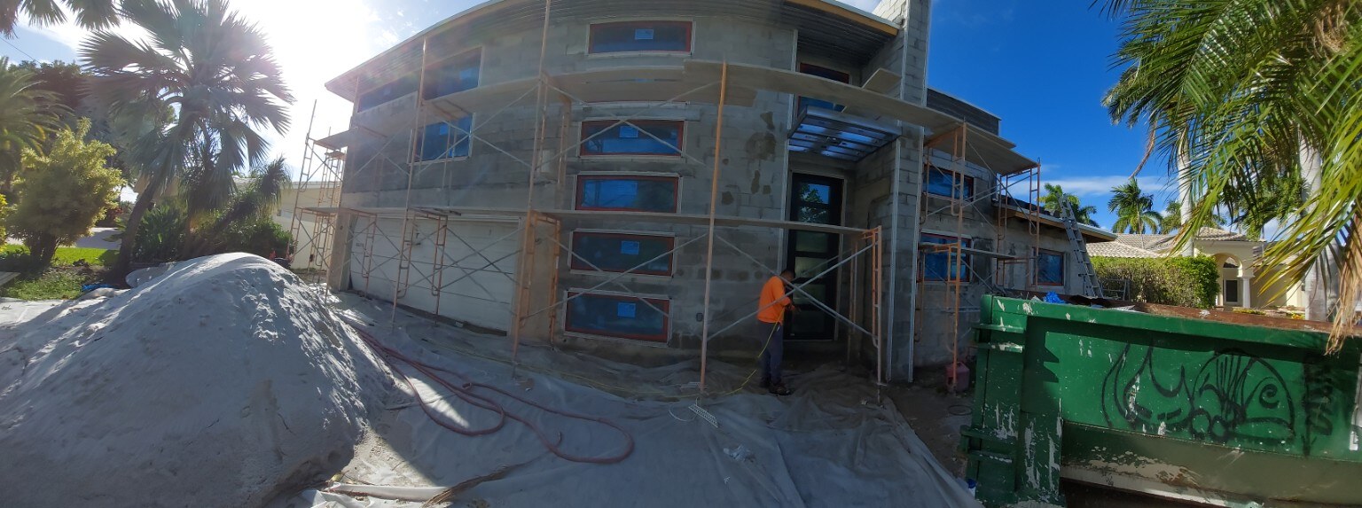 New smooth stucco installation in progress — worker applying base coat over concrete-block modern home with scaffolding in St. Petersburg, FL — H Calix Stucco Design & Paint LLC.